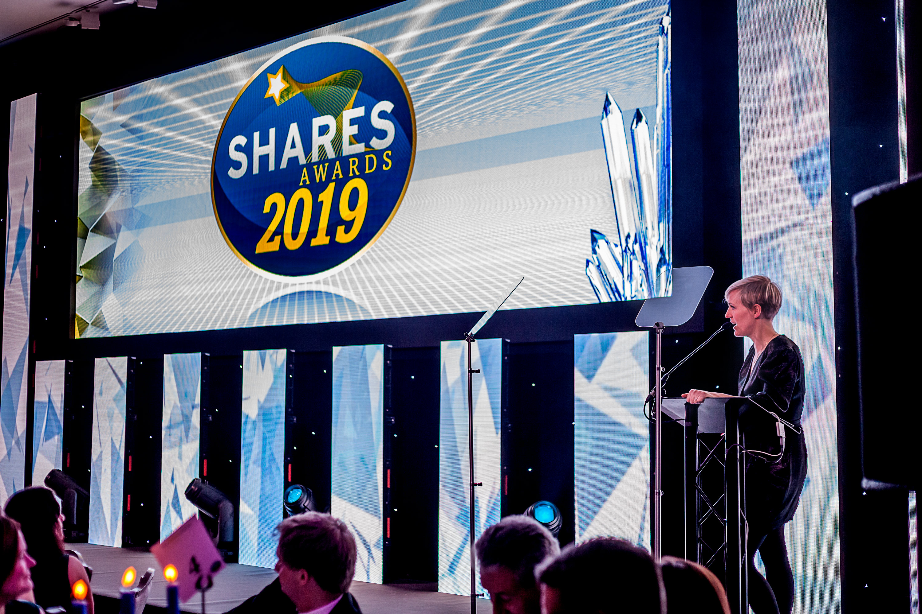 Shares awards ceremony with speaker at podium and attendees