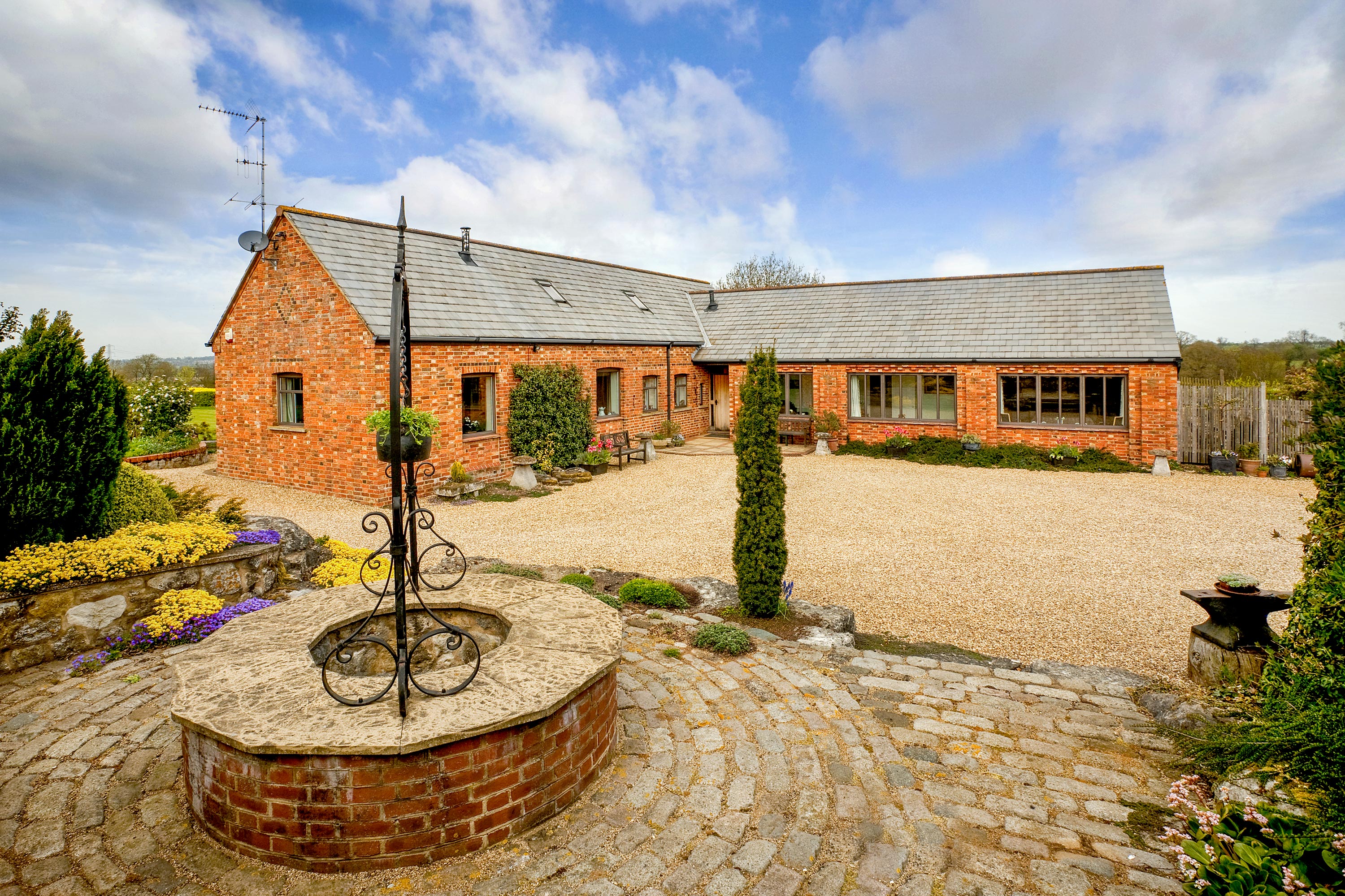 External home photography showcasing l-shaped property with brick paving and a well feature for listing
