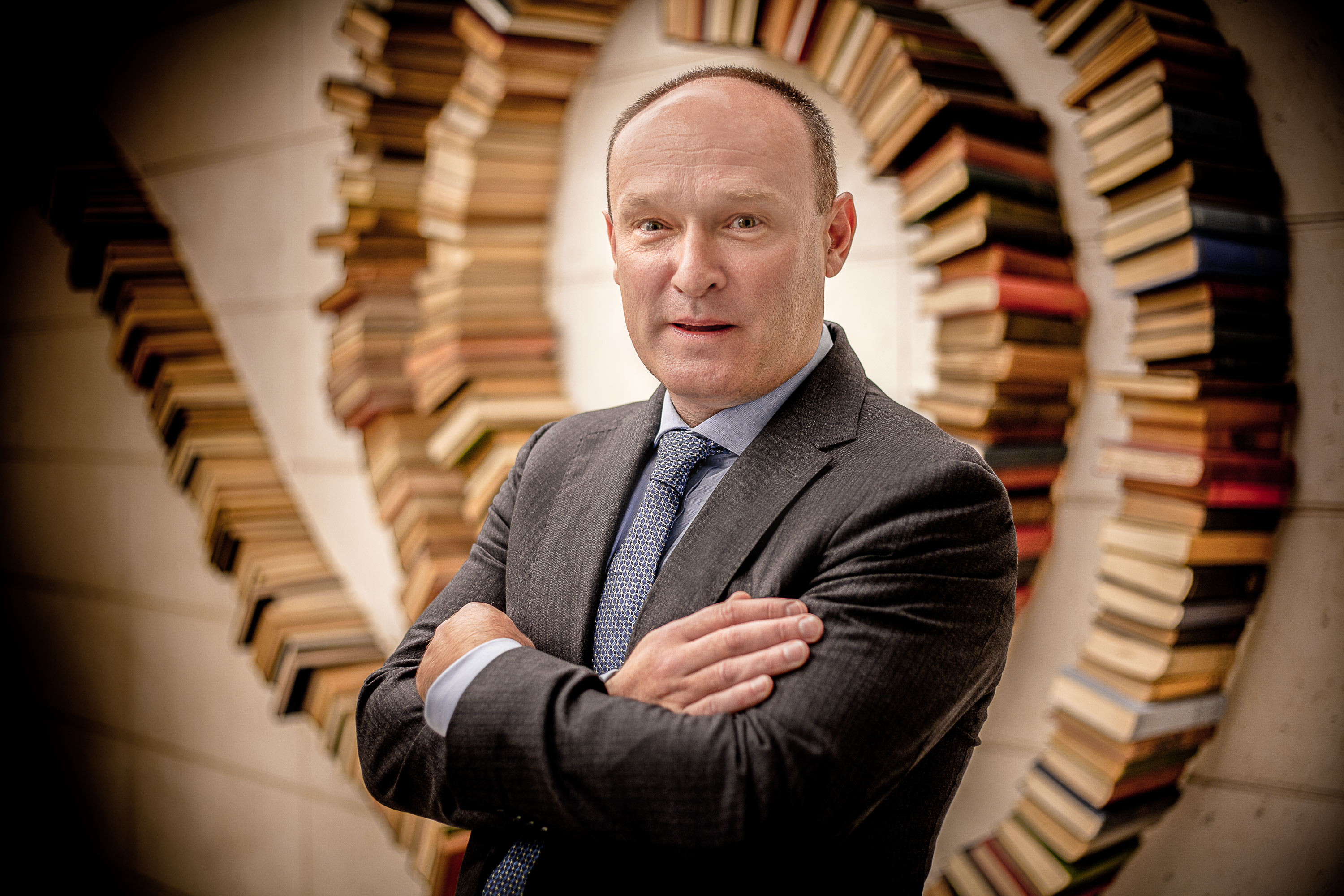 Vignetted staff photo of man wearing a suit in front of a wall of books