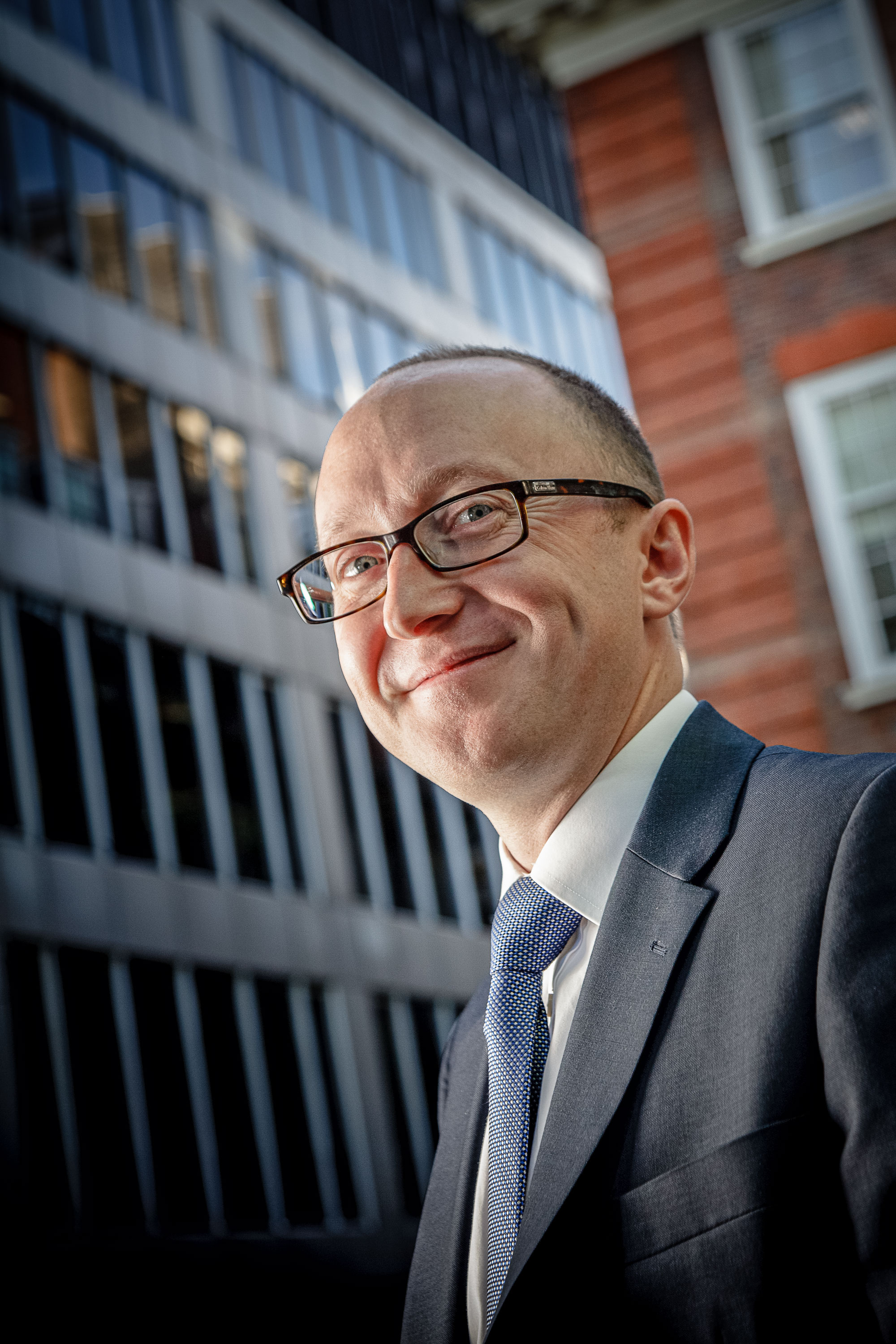 A side lit portrait of a man in front of an office building taken from a low angle by the photographer