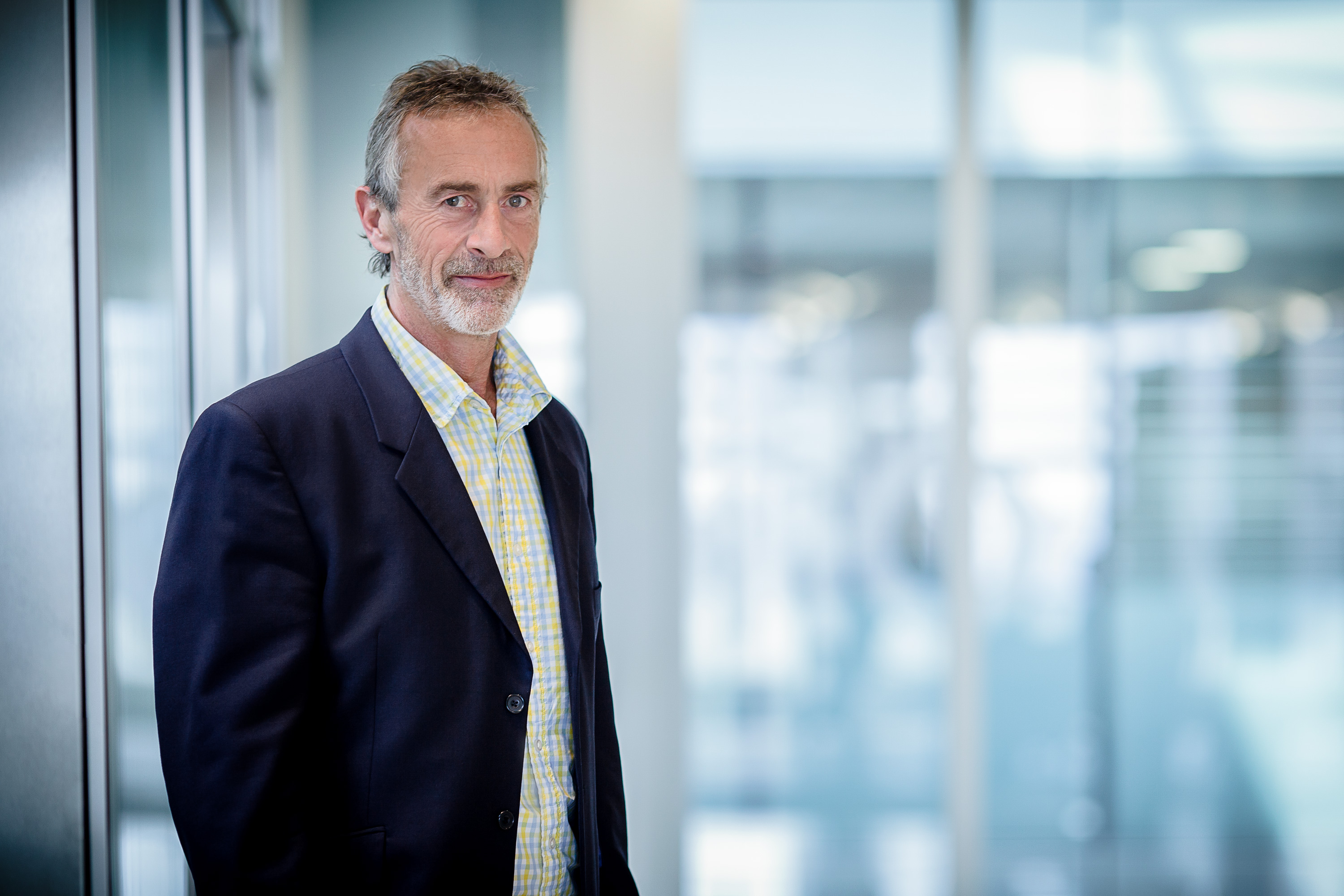 A corporate employee portrait of a suited man with a diffused blue office background