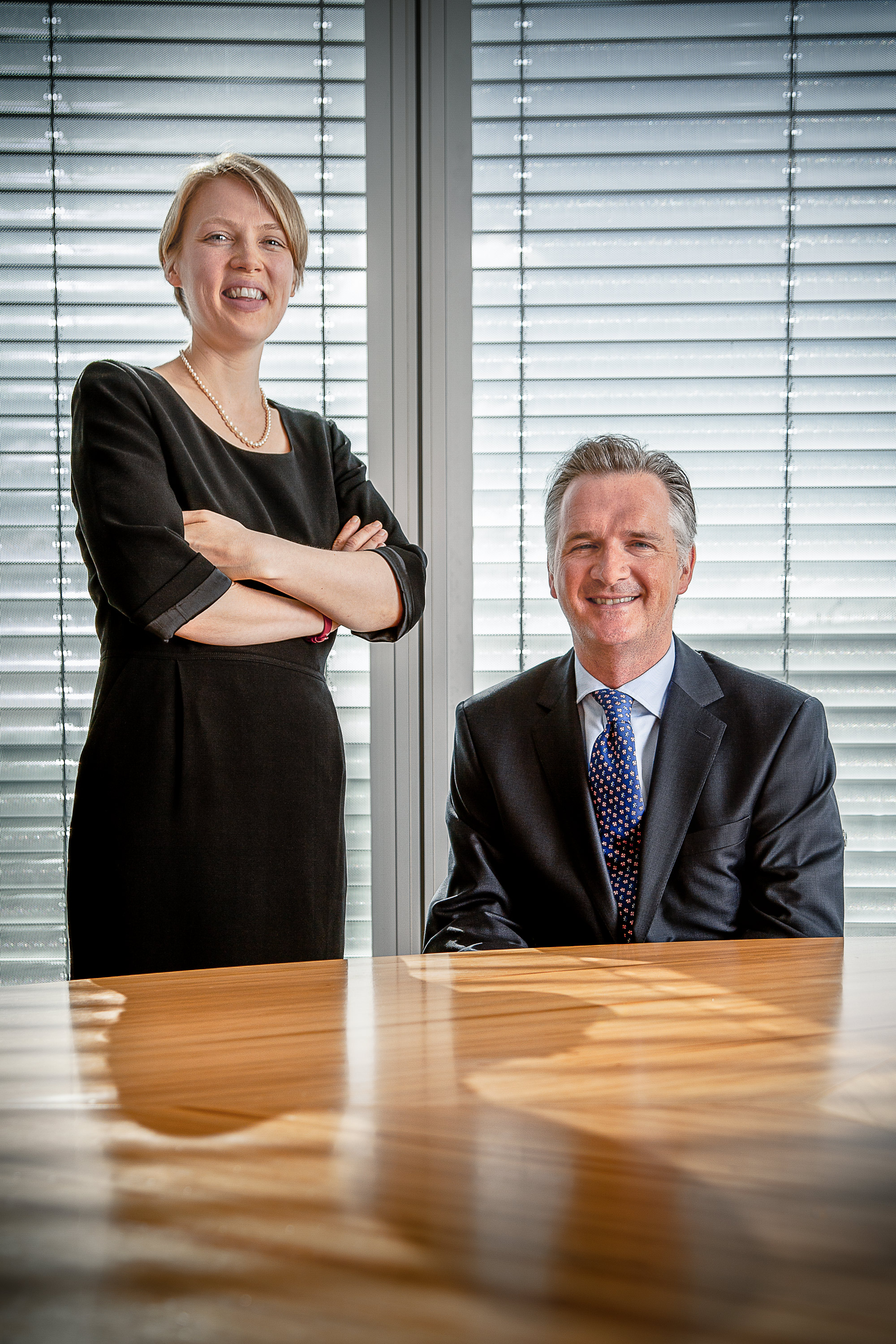 Smiling corporate team photo with two people reflected by shadows on the board room table