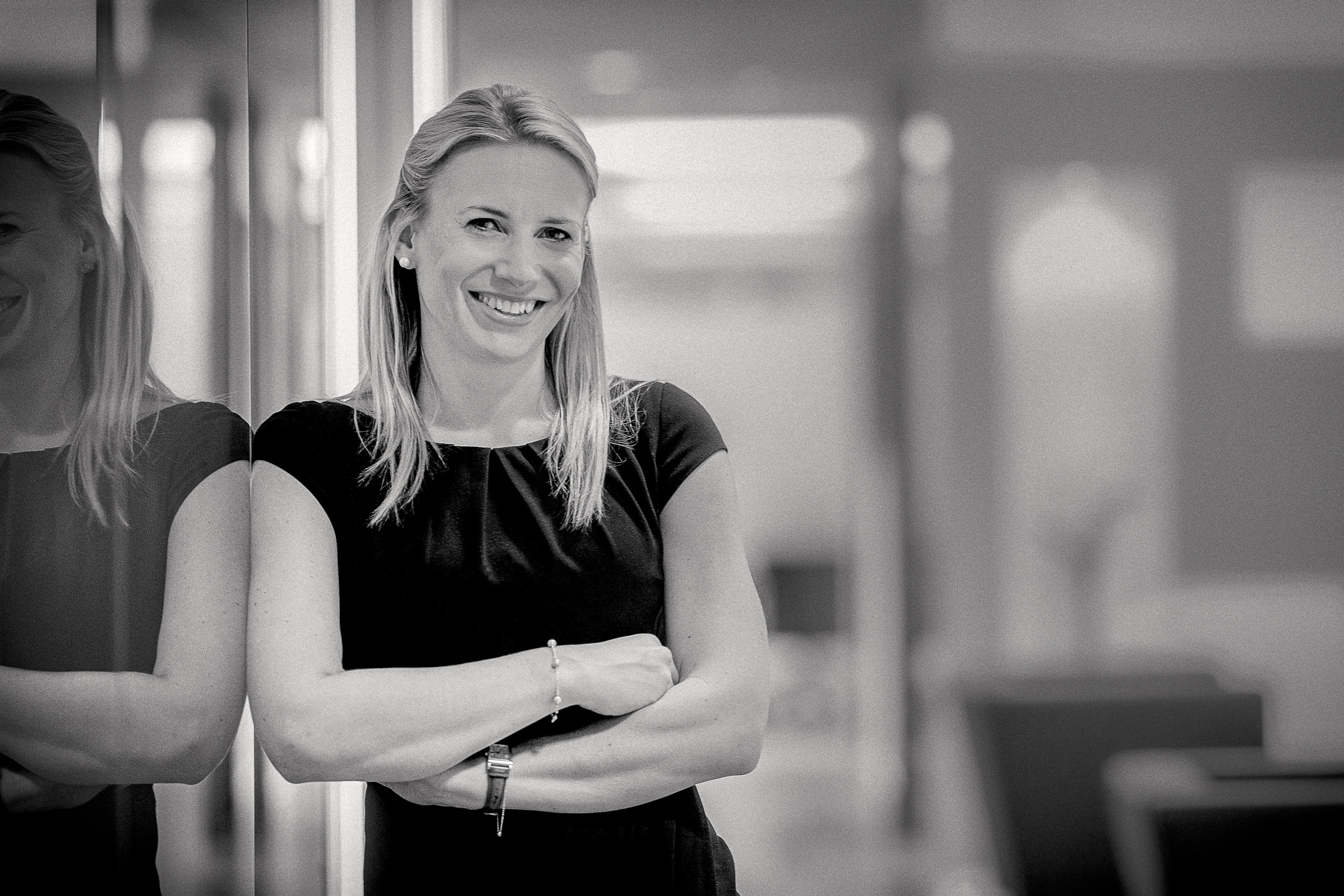 Black and white photography of a smiling woman in a black dress, reflected in the glass
